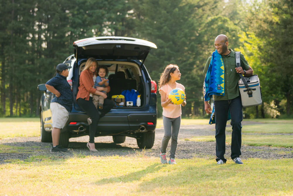 Family unloading gear from the rear hatch of a Subaru SUV at a park