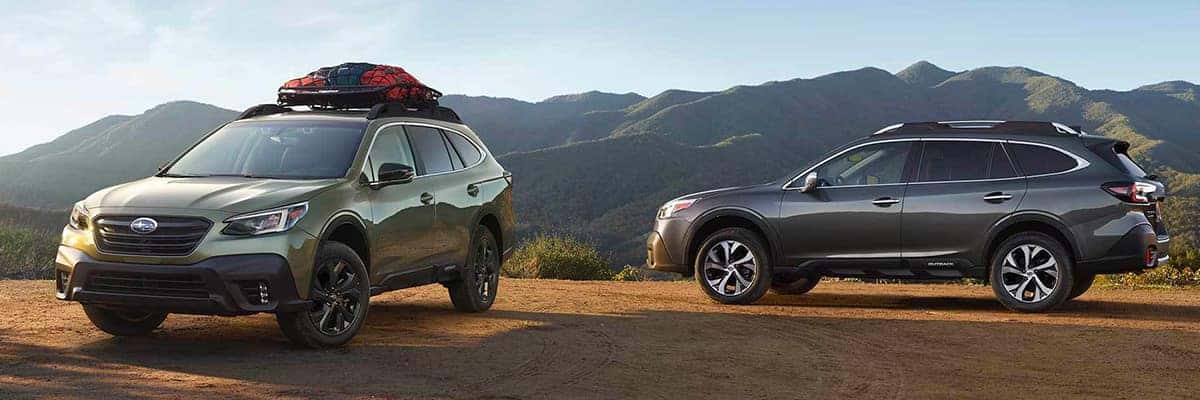 Two Subaru Outback wagons, one with a roof cargo box, parked on a hillside overlooking mountains