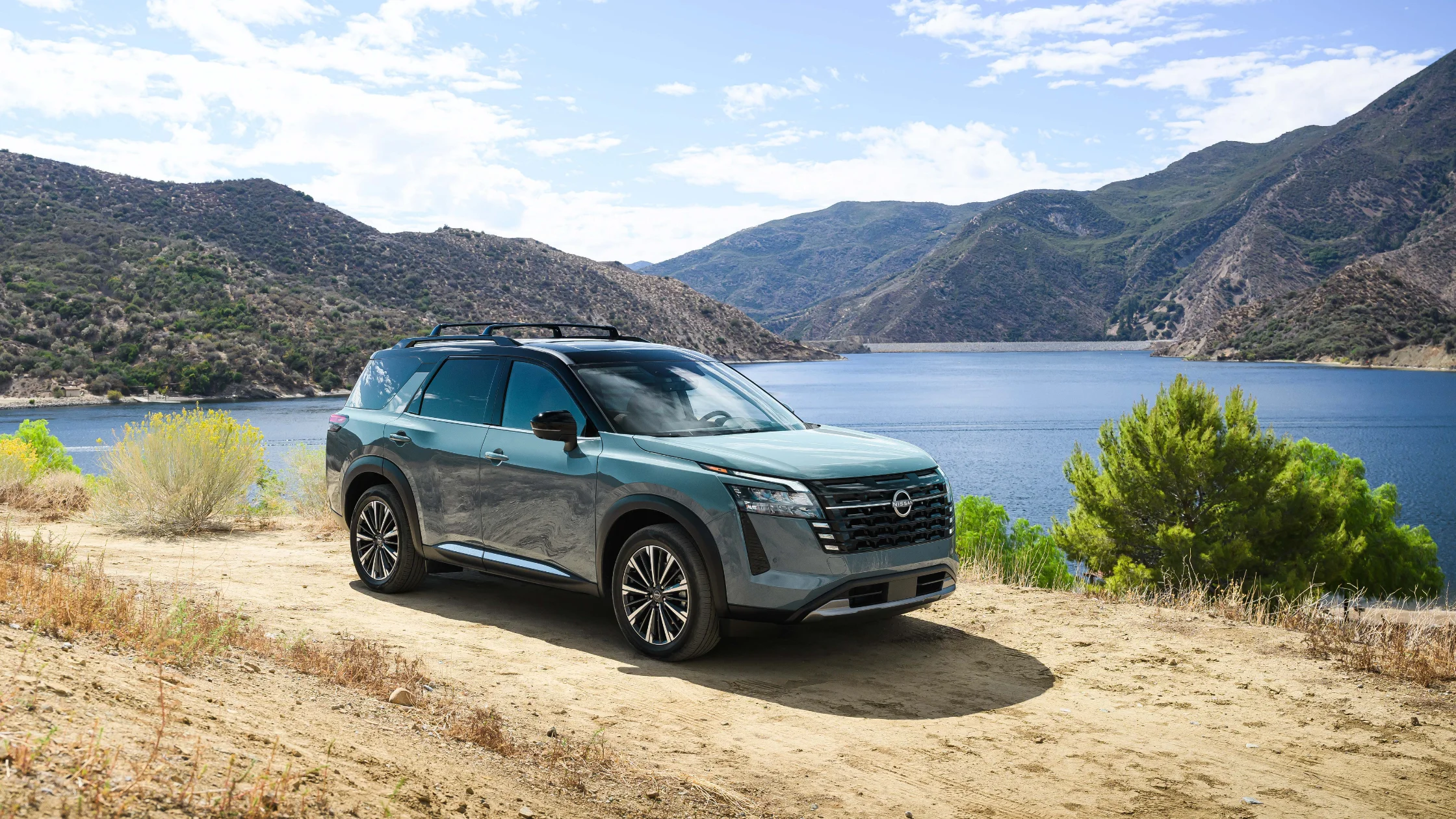 2026 Nissan Pathfinder® gray SUV parked by mountain lake with roof rails and rugged scenery
