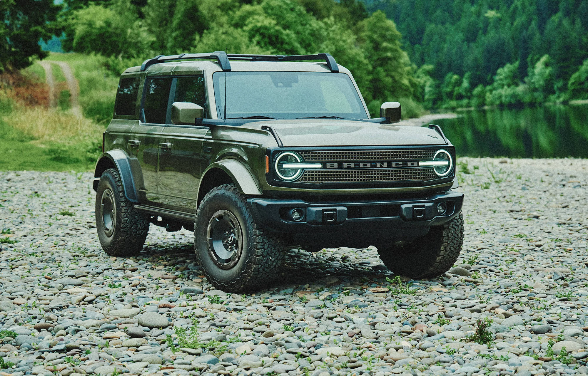 2027 Ford Bronco four-door in green parked on a rocky riverbank