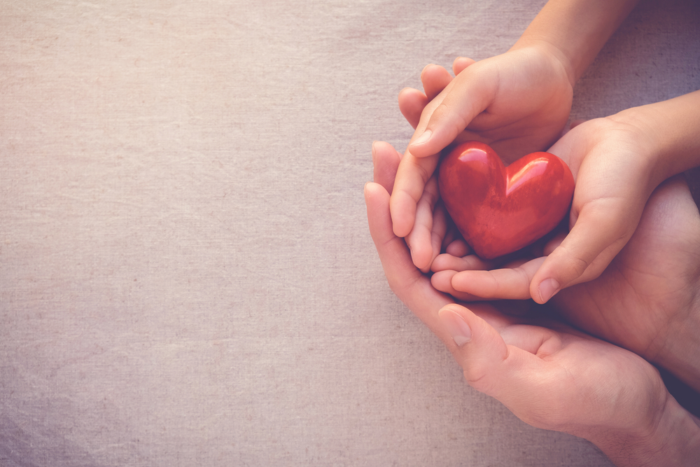 heart resting on a child's hands while child's hands are resting on adult's hands, all palms up