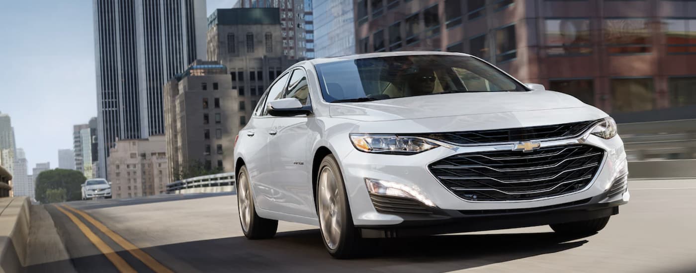 White 2021 Chevy Malibu driving down a city street.