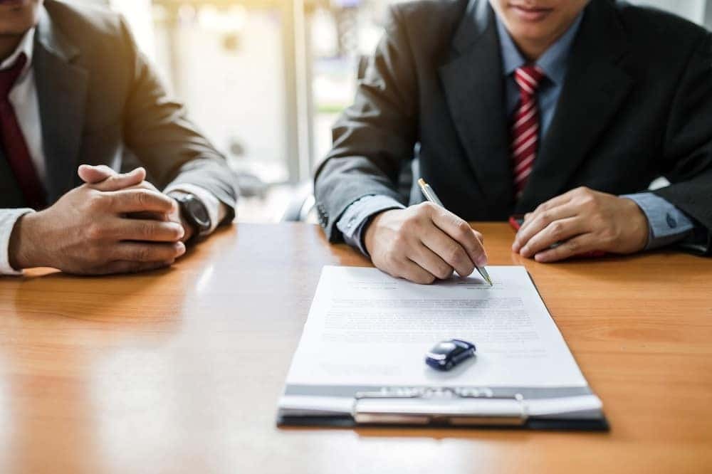Two people at a desk signing vehicle paperwork with a toy car on the contract