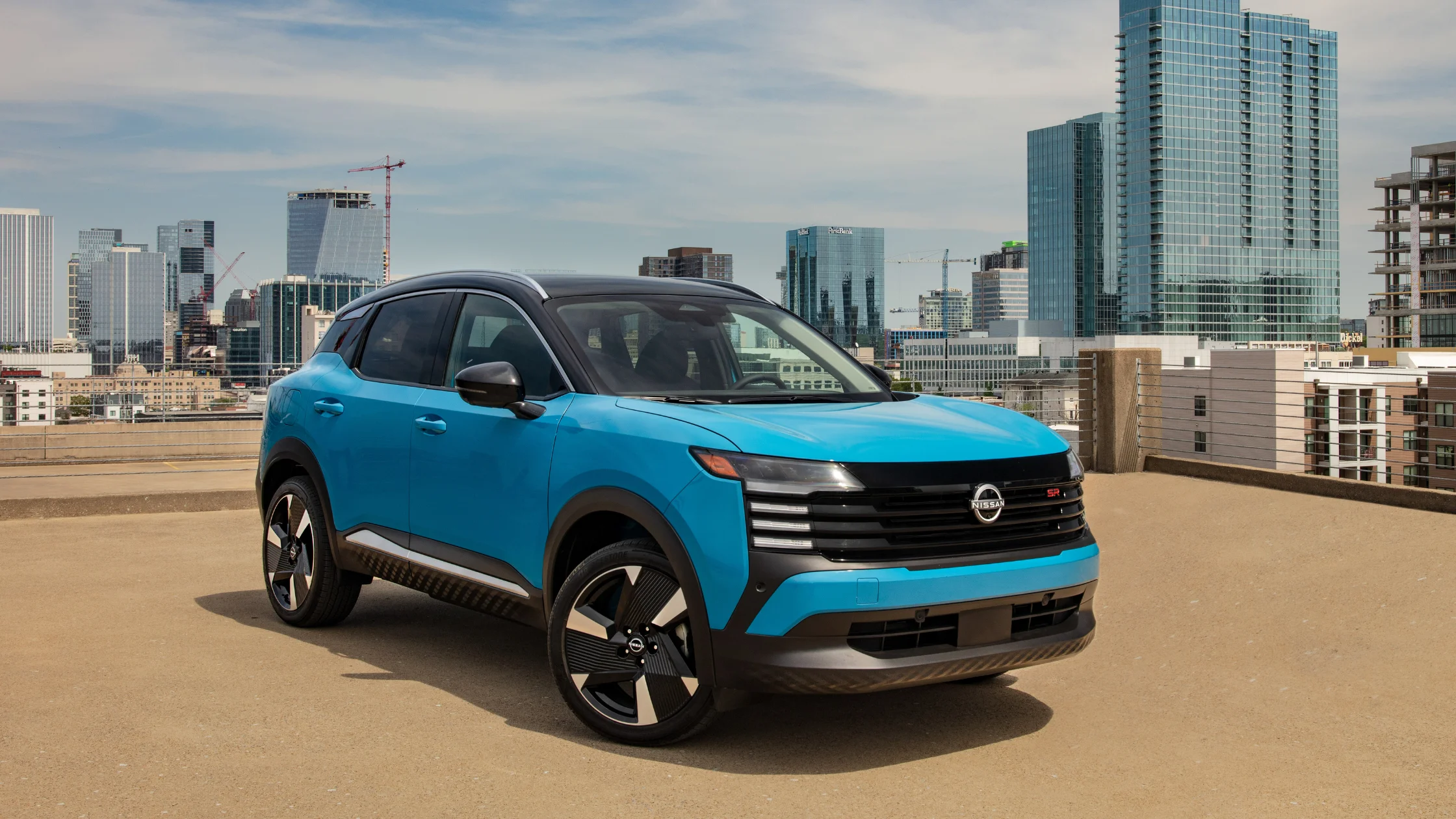 2026 Nissan Kicks® SR in bright blue parked on a rooftop with a modern urban city skyline behind it.