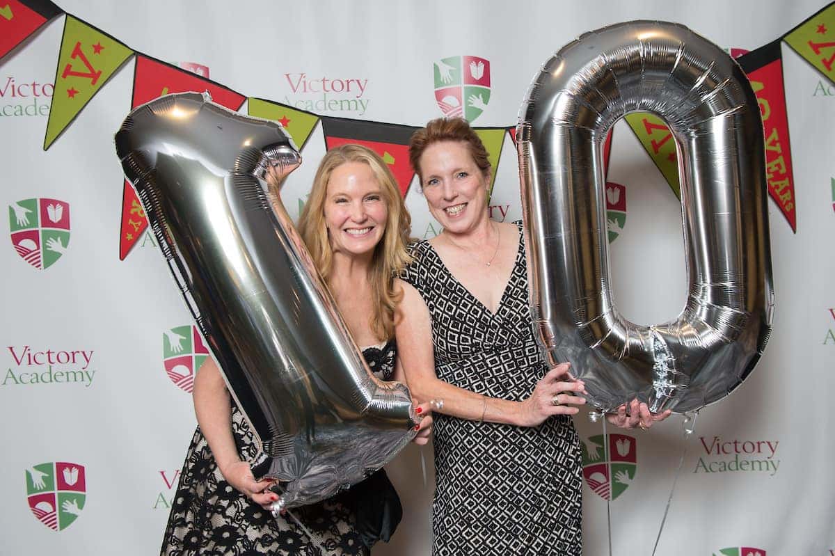 Two women holding number 10 balloons at a Victory Academy event