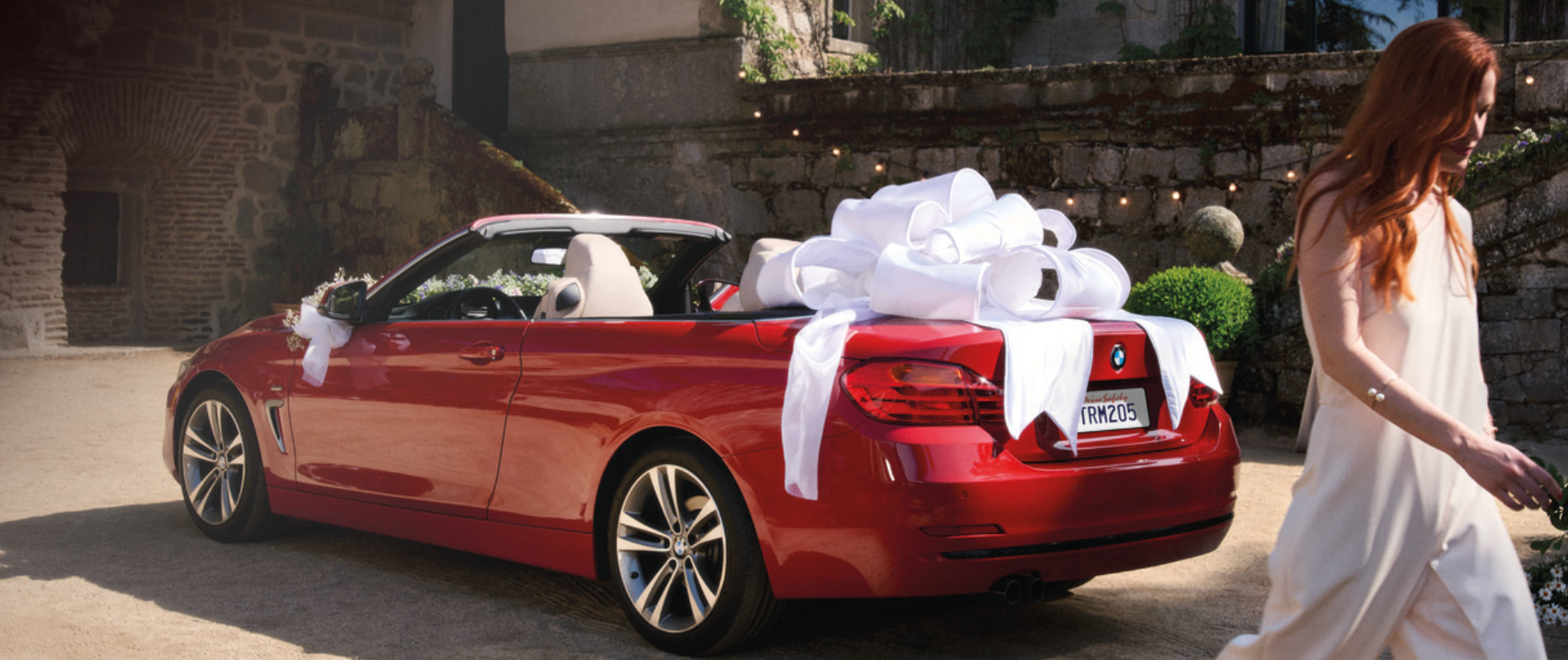 Customer walks near a parked BMW 4 Series decorated with a large white ribbon bow on the trunk.