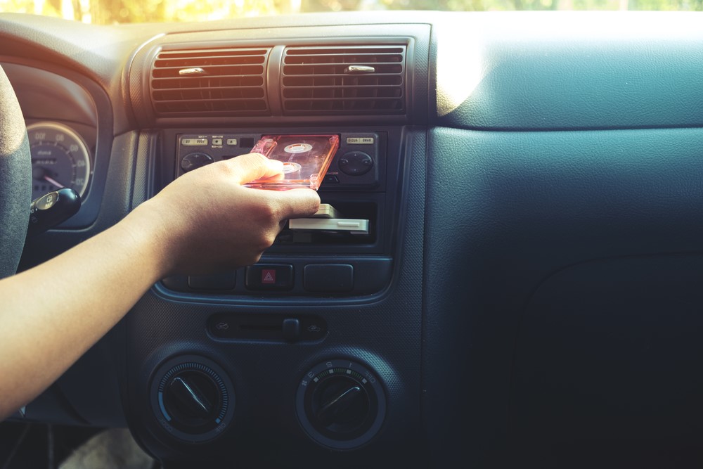 A person’s hand inserting a cassette tape into a car’s cassette player, emphasizing the tactile interaction of using a cassette player.