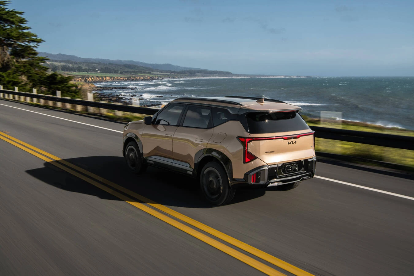 Gold Kia Seltos driving along a coastal highway with ocean and cliffs in the background