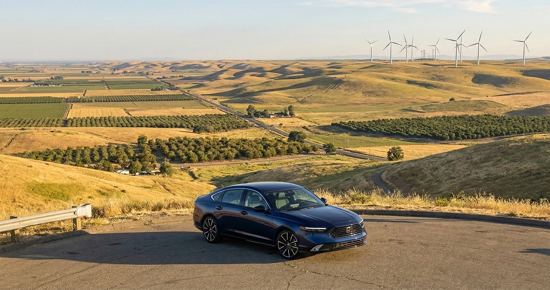 Blue Honda Accord sedan parked on a scenic overlook above rolling farmland and wind turbines near Tracy, California