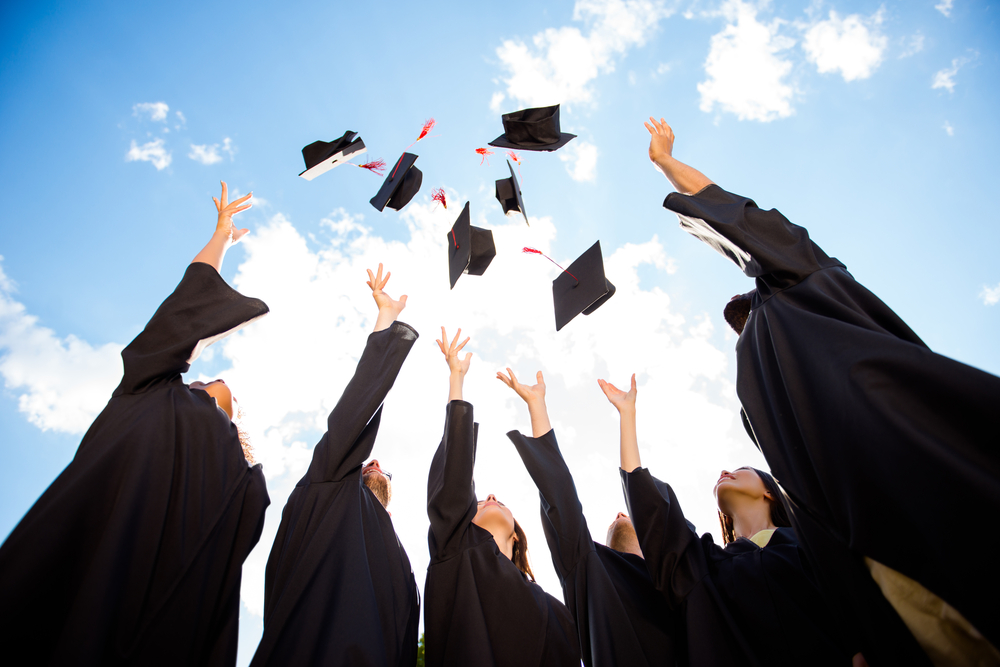 graduates dressed in gowns tossing their caps towards the sky