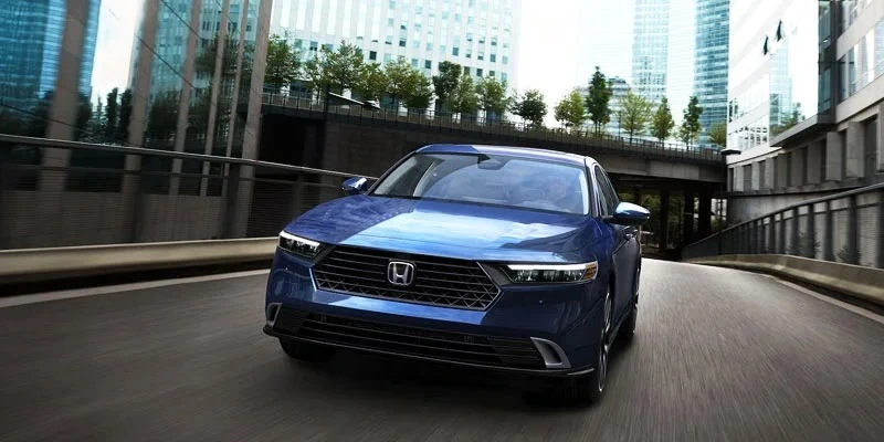 Blue Honda sedan driving on a city road with skyscrapers in background.