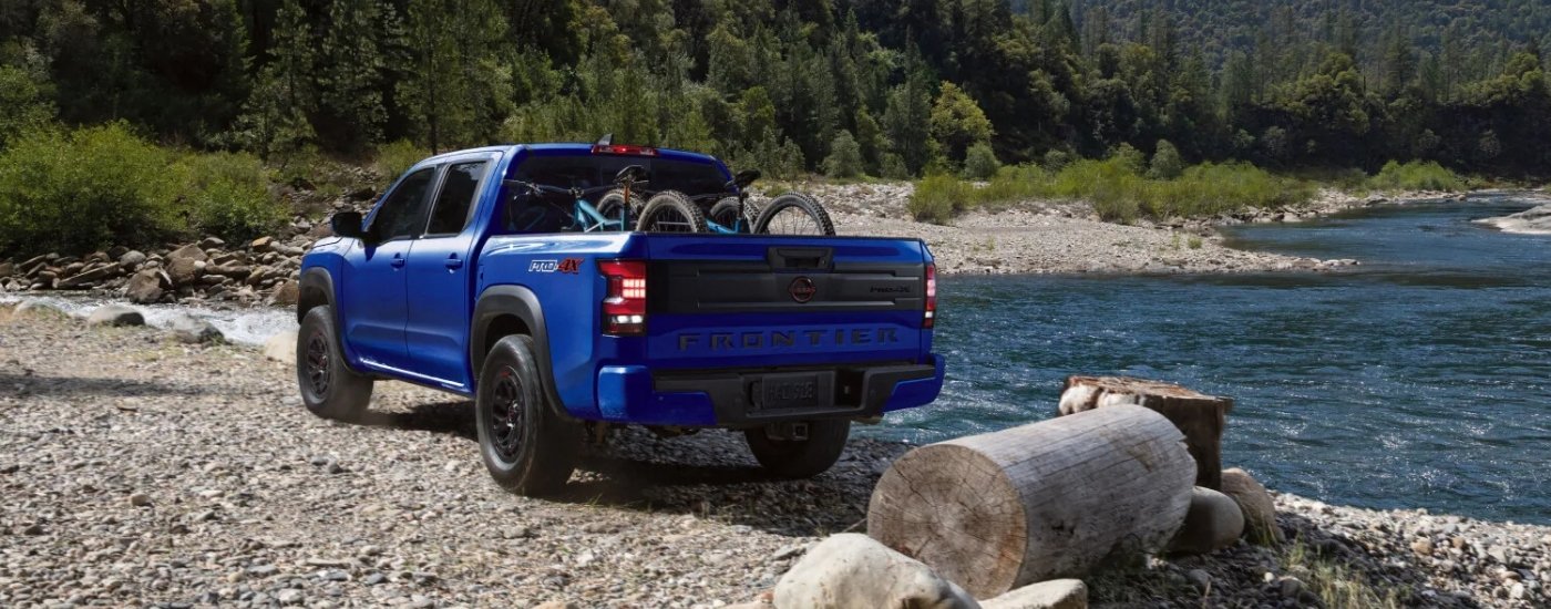 Blue 2026 Nissan Frontier PRO-4X parked next to a river with mountain bikes in the bed