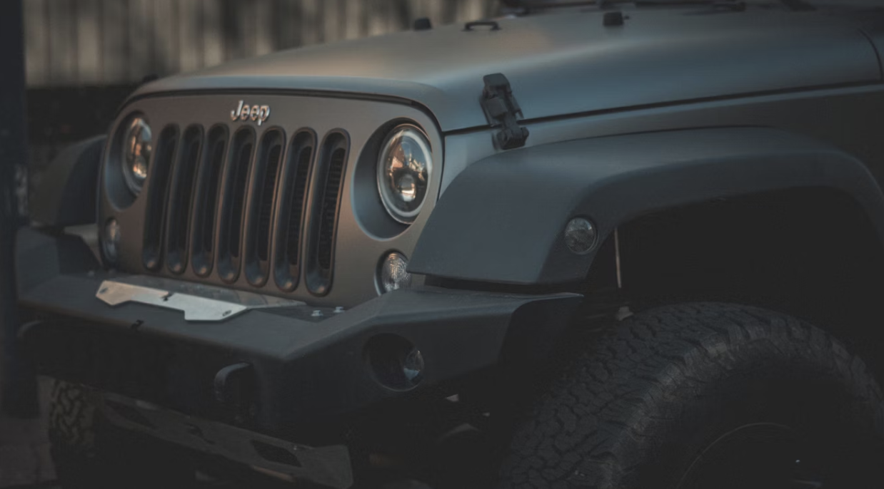 Close-up of the front grille and headlight of a gray Jeep Wrangler with an aftermarket bumper.