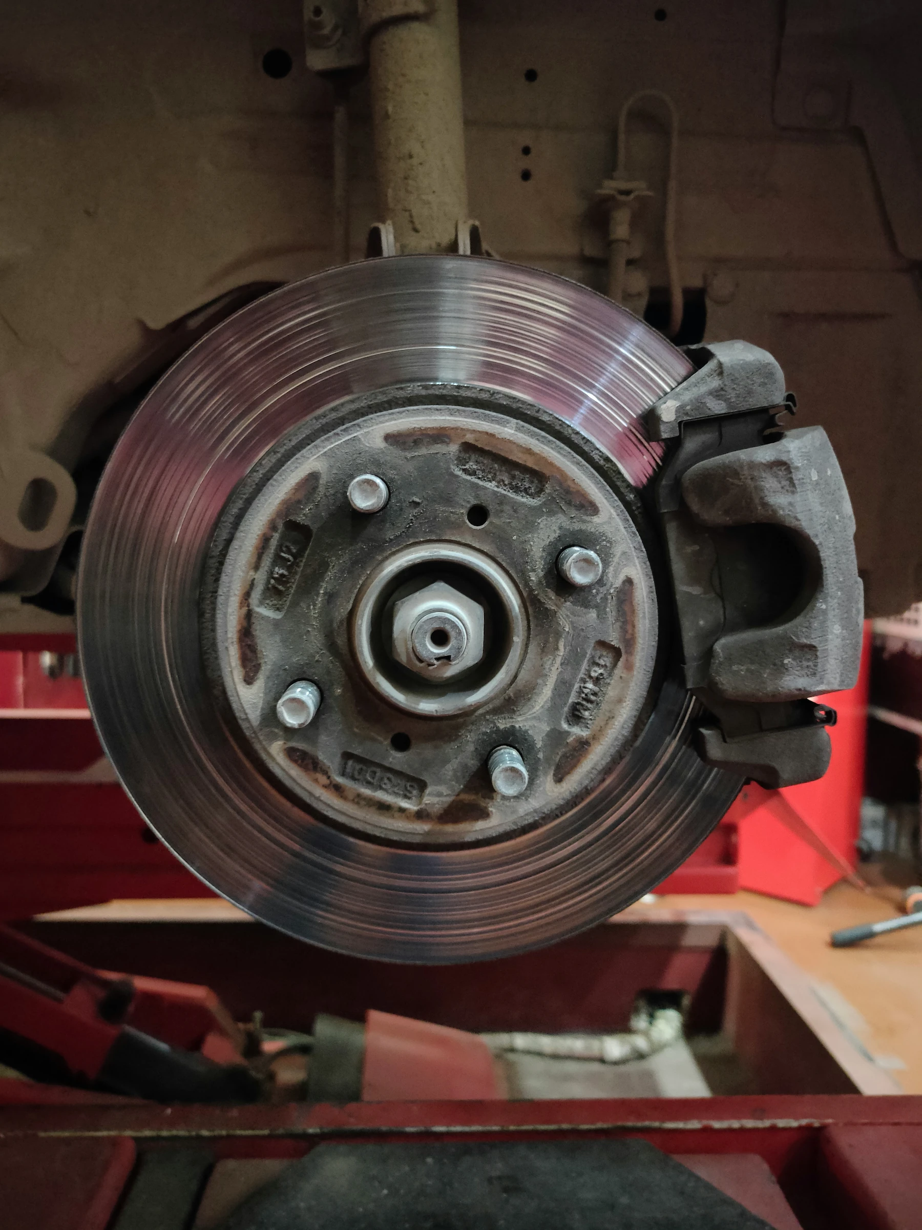 Close-up of a vehicle's front brake rotor and caliper on a shop lift during a brake repair inspection