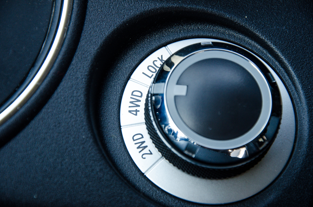 Zoomed in image of a knob on a car that has 3 options on it, one for 4WD, one for 2WD and one for Lock, the interior of the car is black and the knob is silver