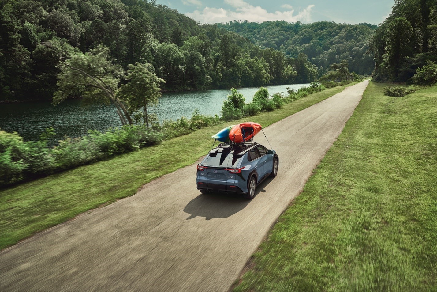 A Subaru Solterra with a Thule cargo carrier drives over a wooded gorge.