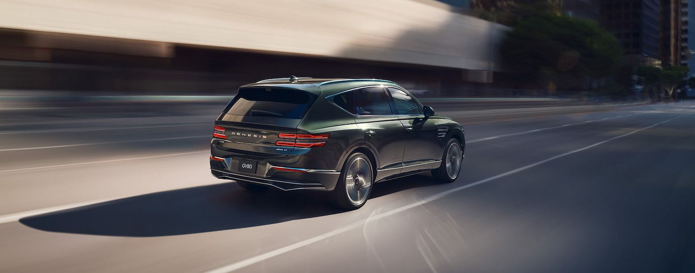 Rear of a green 2025 Genesis GV80 driving down a road.