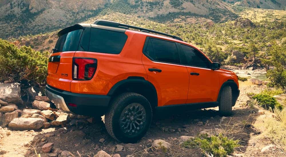 Rear view of an orange 2026 Honda Passport TrailSport Elite driving down a steep cliff.