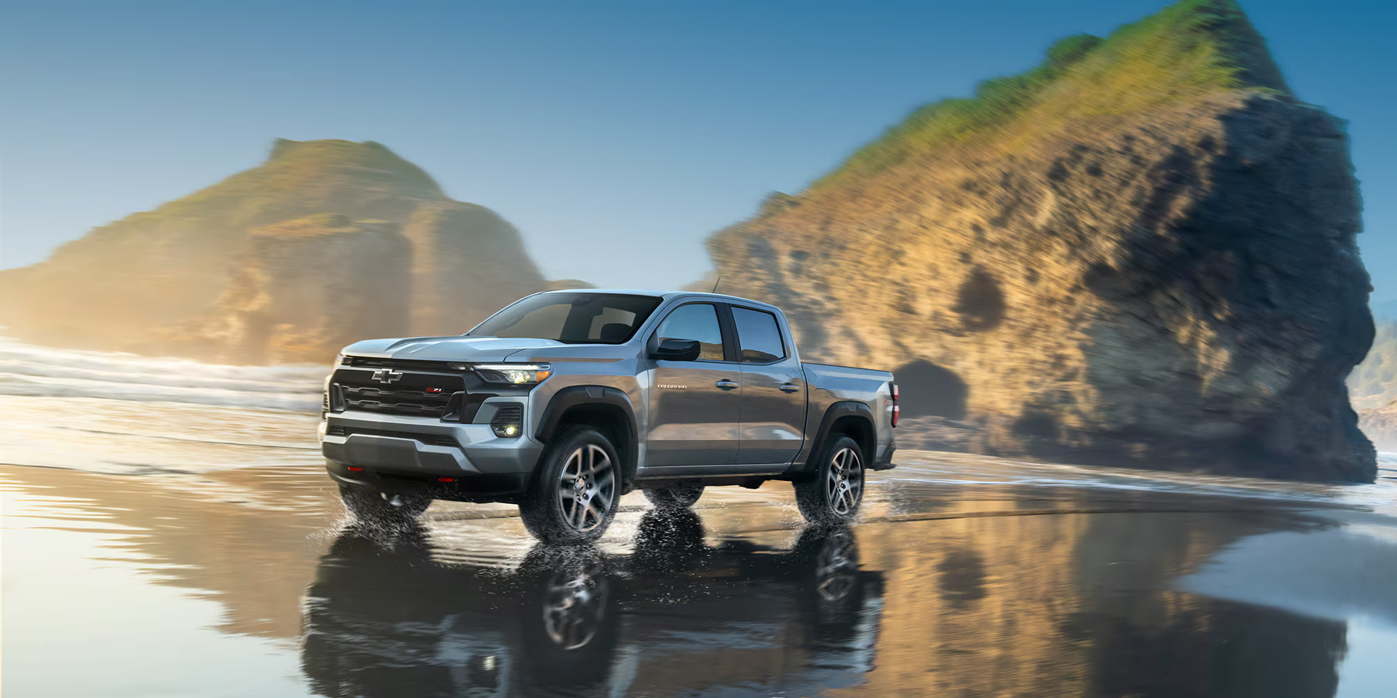 A silver truck driving on the beach.