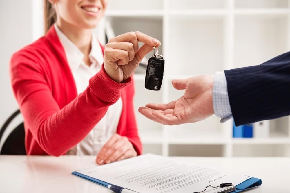 Salesperson handing car keys to a customer across a desk