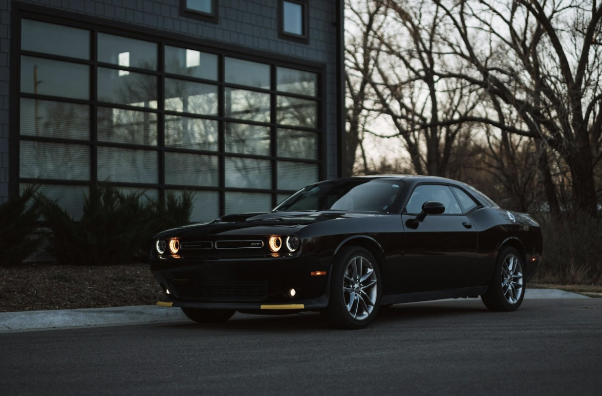 A black Dodge Challenger R/T parked on asphalt outside a modern building at dusk.