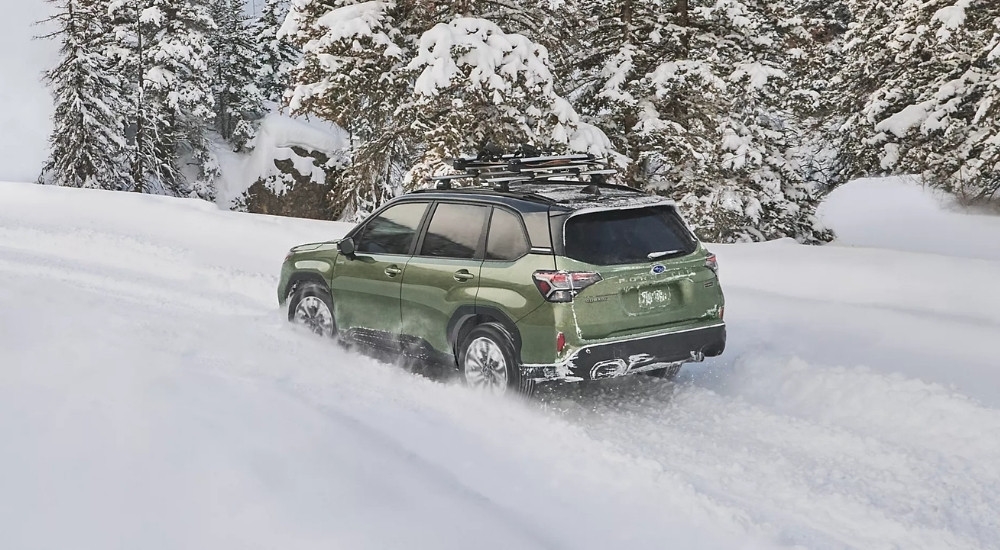 A green 2025 Subaru Forester Hybrid driving on a snowy street.