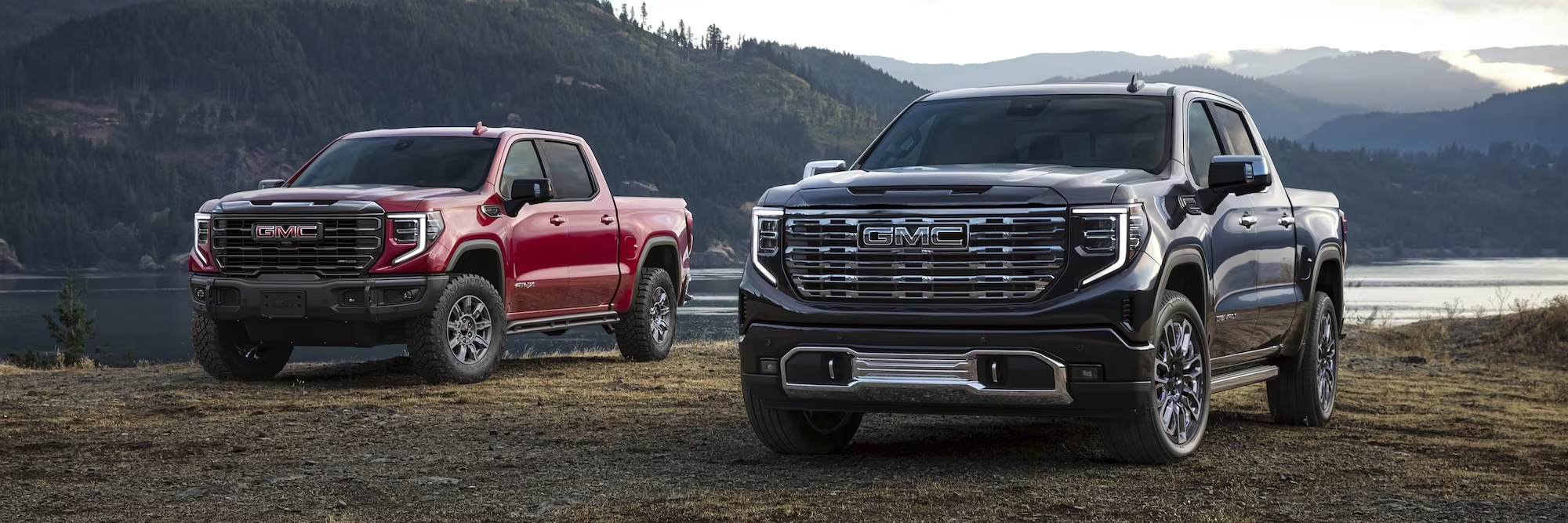 Front View of Two 2026 GMC Sierra 1500 Pickup Trucks Parked in a Grassy Field by a Body of Water