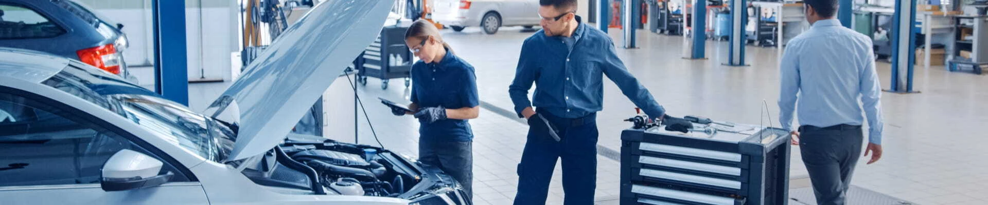 Automotive technicians inspecting a vehicle with its hood open inside a service center.