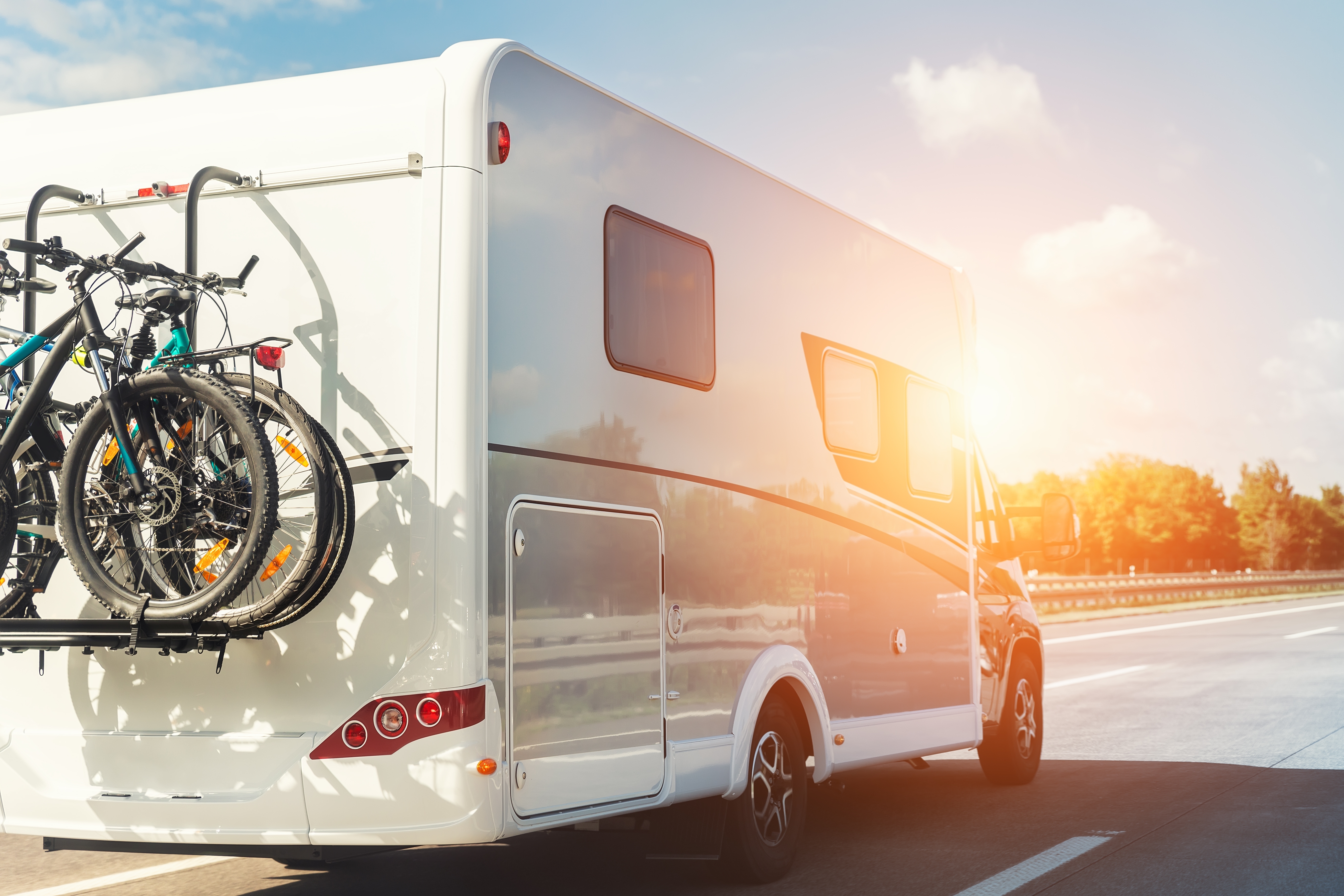 RV motorhome, with bikes mounted on the back of it, driving down the highway on a sunny day