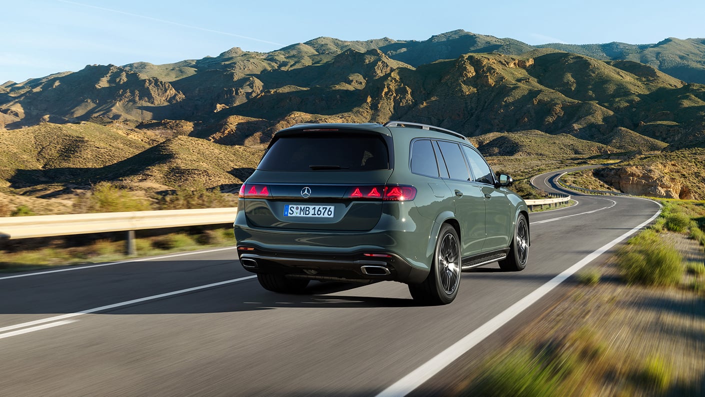 2027 Mercedes-Benz GLS in green driving on a winding mountain road, rear view
