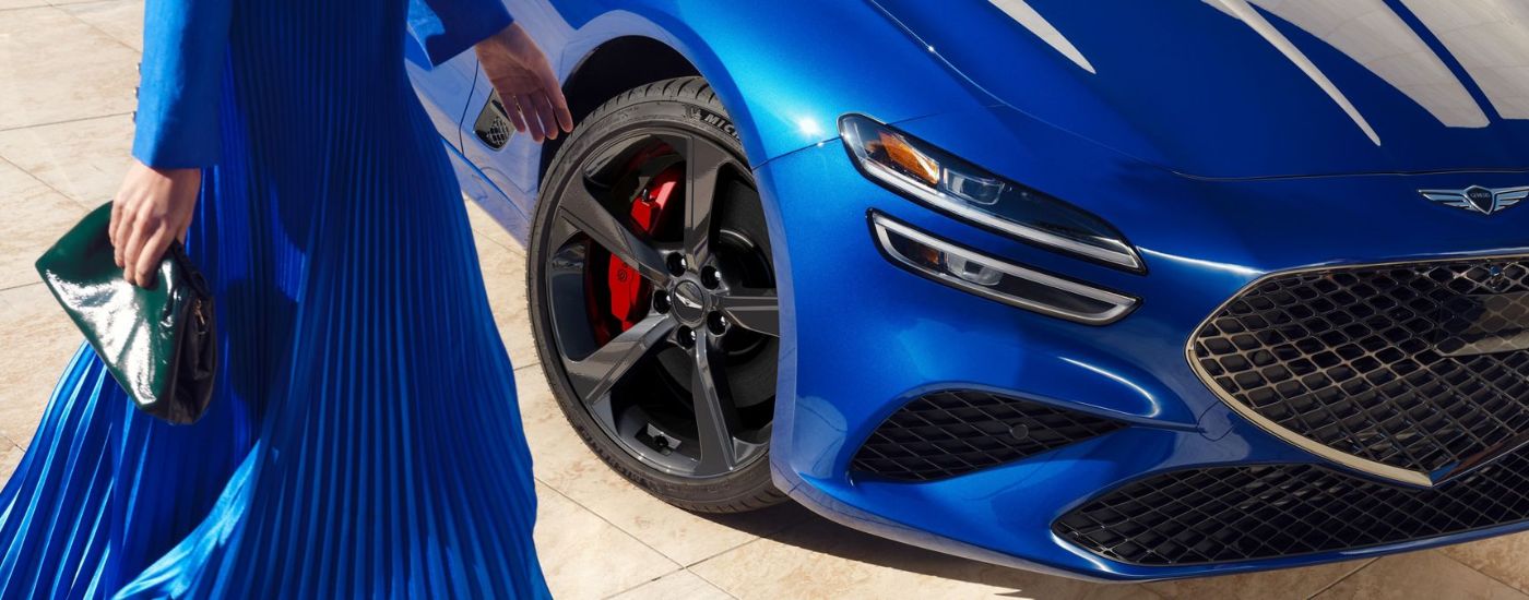 A woman standing by a blue 2026 Genesis G70.