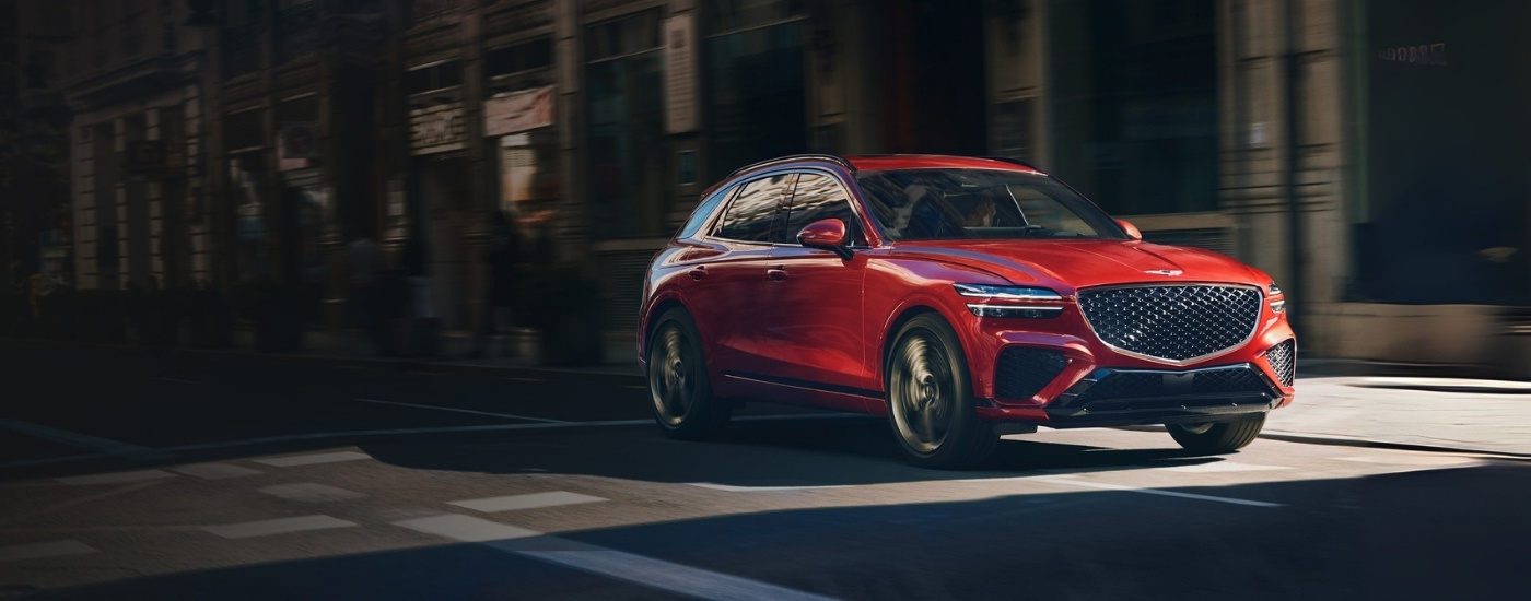 Red 2023 Genesis GV70 driving past shops