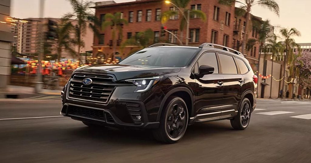 Black 2025 Subaru Ascent driving down a city street at dusk