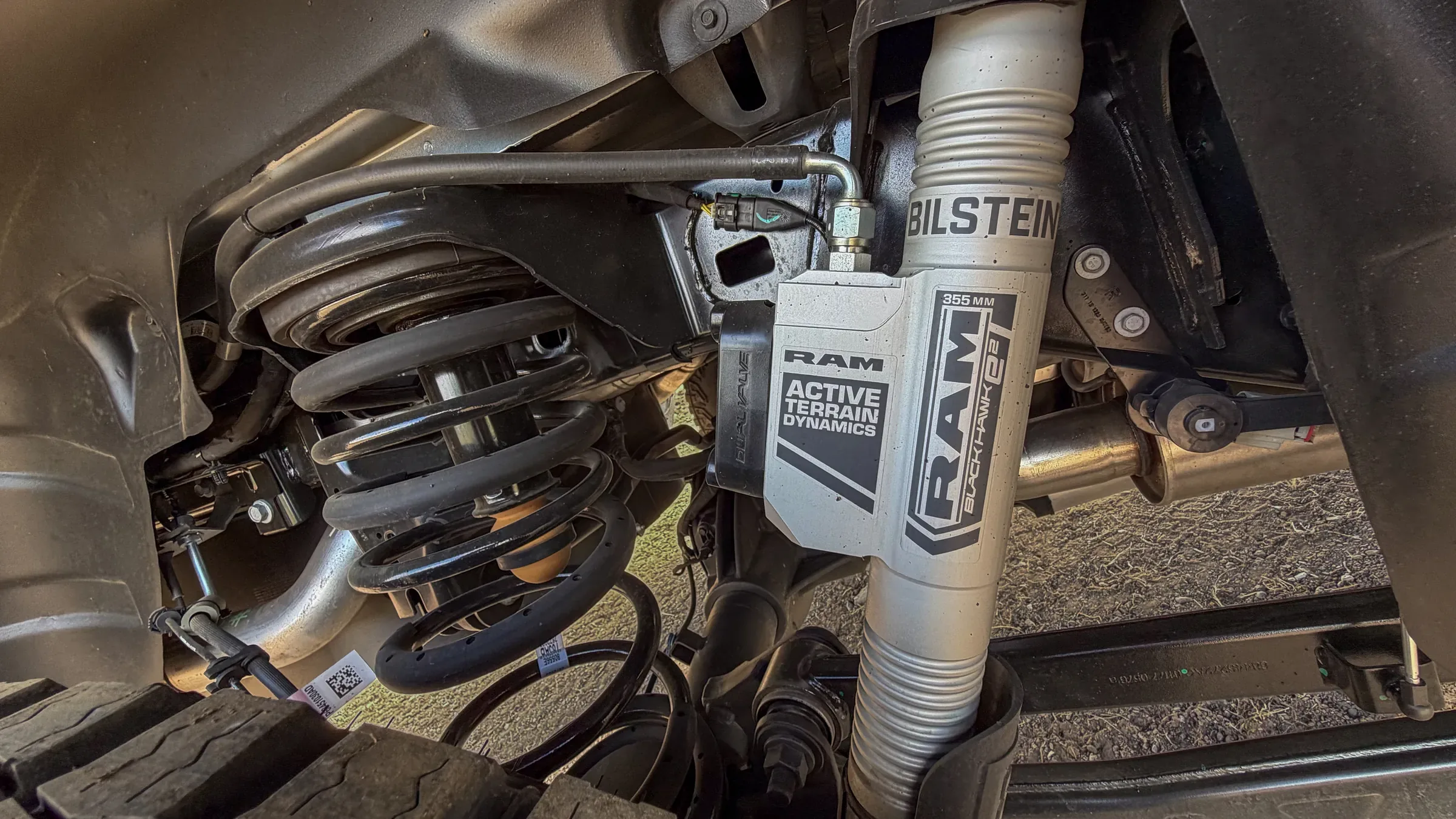 Underside view of a Ram truck's front suspension showing a Bilstein Blackhawk e2 shock absorber labeled Ram Active Terrain Dynamics. Shocks and Struts Service in Kansas City, KS