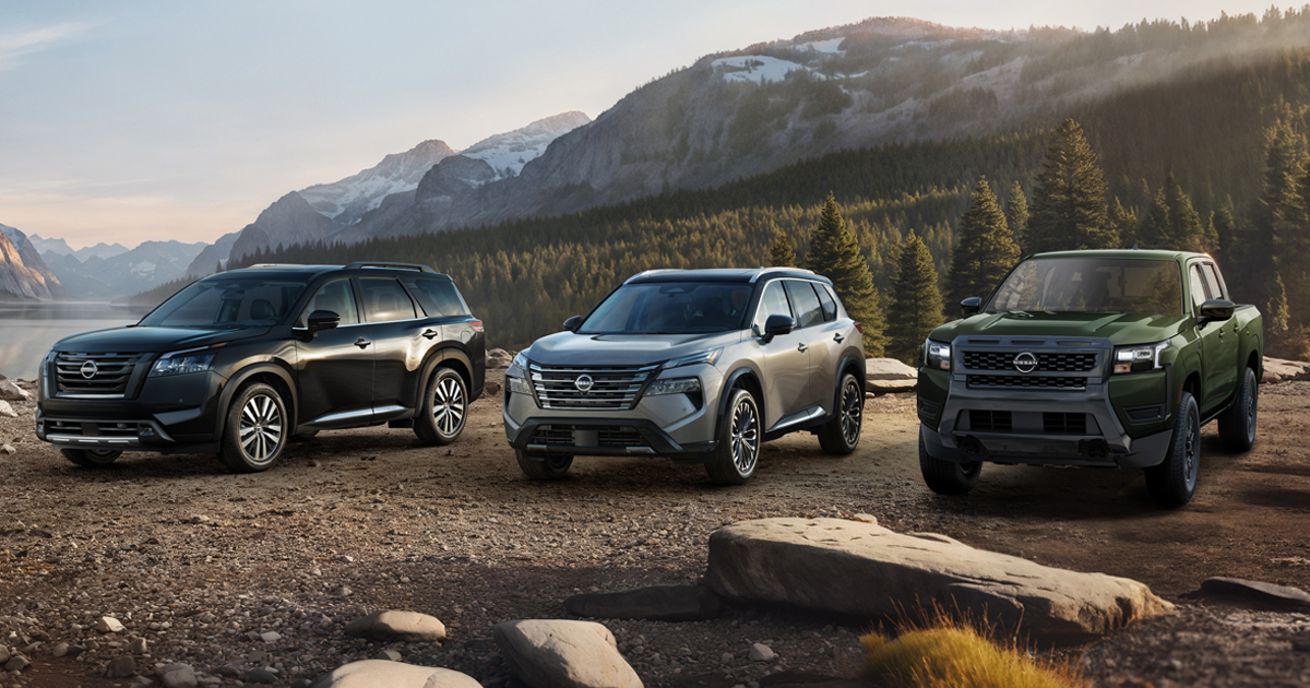 A line-up of several Nissan Models including a Nissan Pathfinder, a Nissan Rogue, and a Nissan Frontier parked off-road at a campsite.