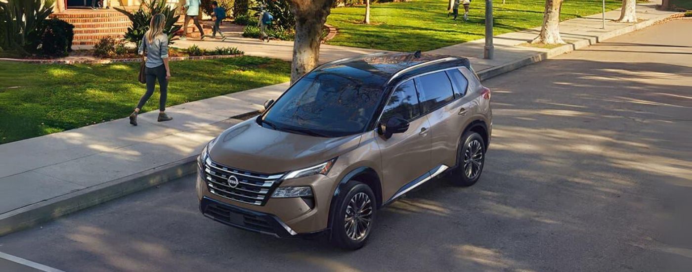 Bronze 2024 Nissan Rogue Platinum parked on the street in front of a school