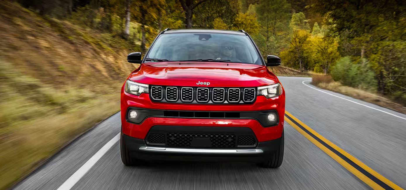 2024 Jeep Compass in vibrant red driving on a scenic curvy road, highlighting its dynamic performance and stylish front grille.