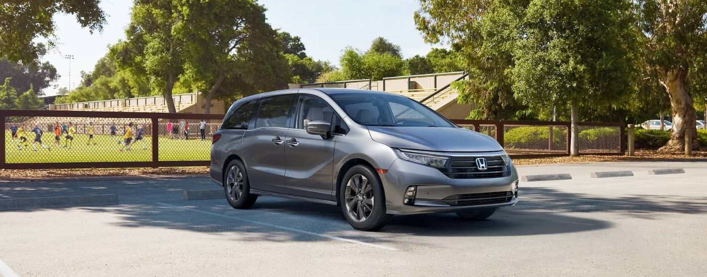A gray 2021 Honda Odyssey is parked in front of a soccer field.
