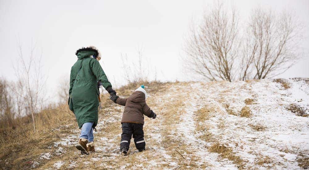 A parent and child are walking on a snowy trail up a hill.