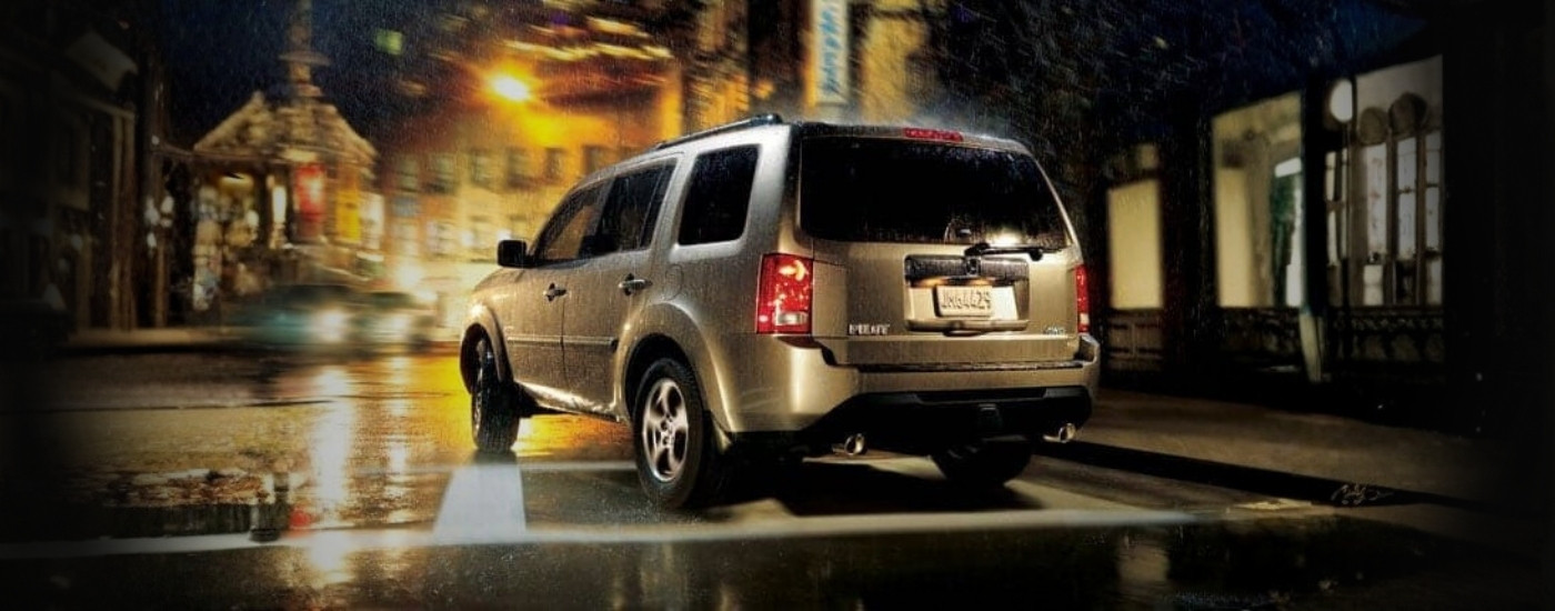 Gold 2012 Honda Pilot driving on a rainy night