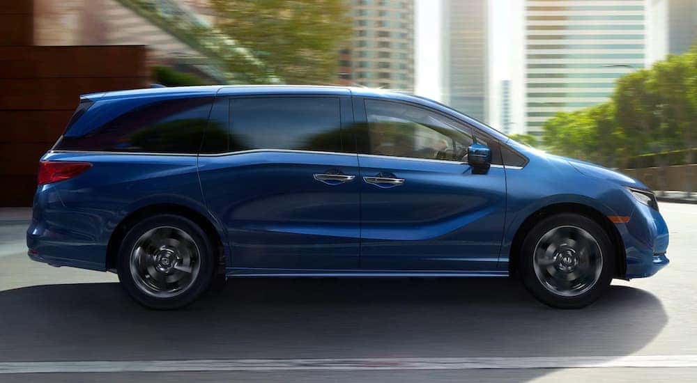 Side angle view of a blue 2025 Honda Odyssey Elite driving through a city.