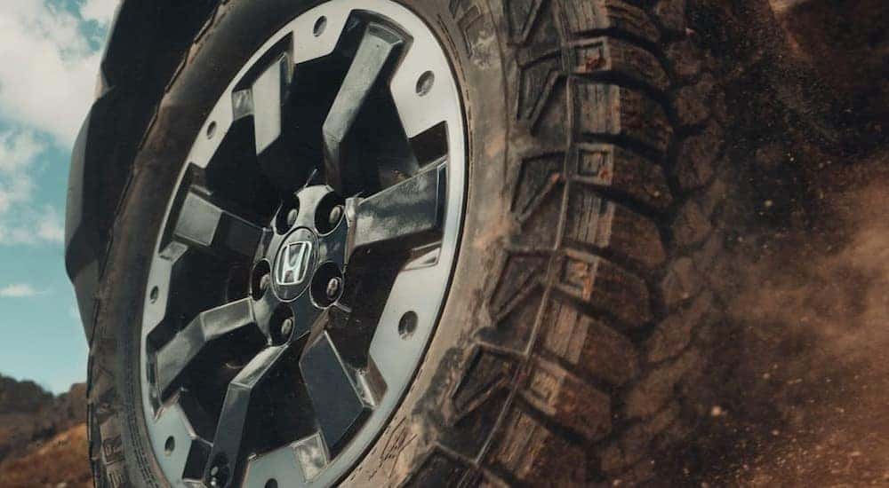 A close-up of the wheel is shown on an orange 2026 Honda Passport TrailSport Elite.