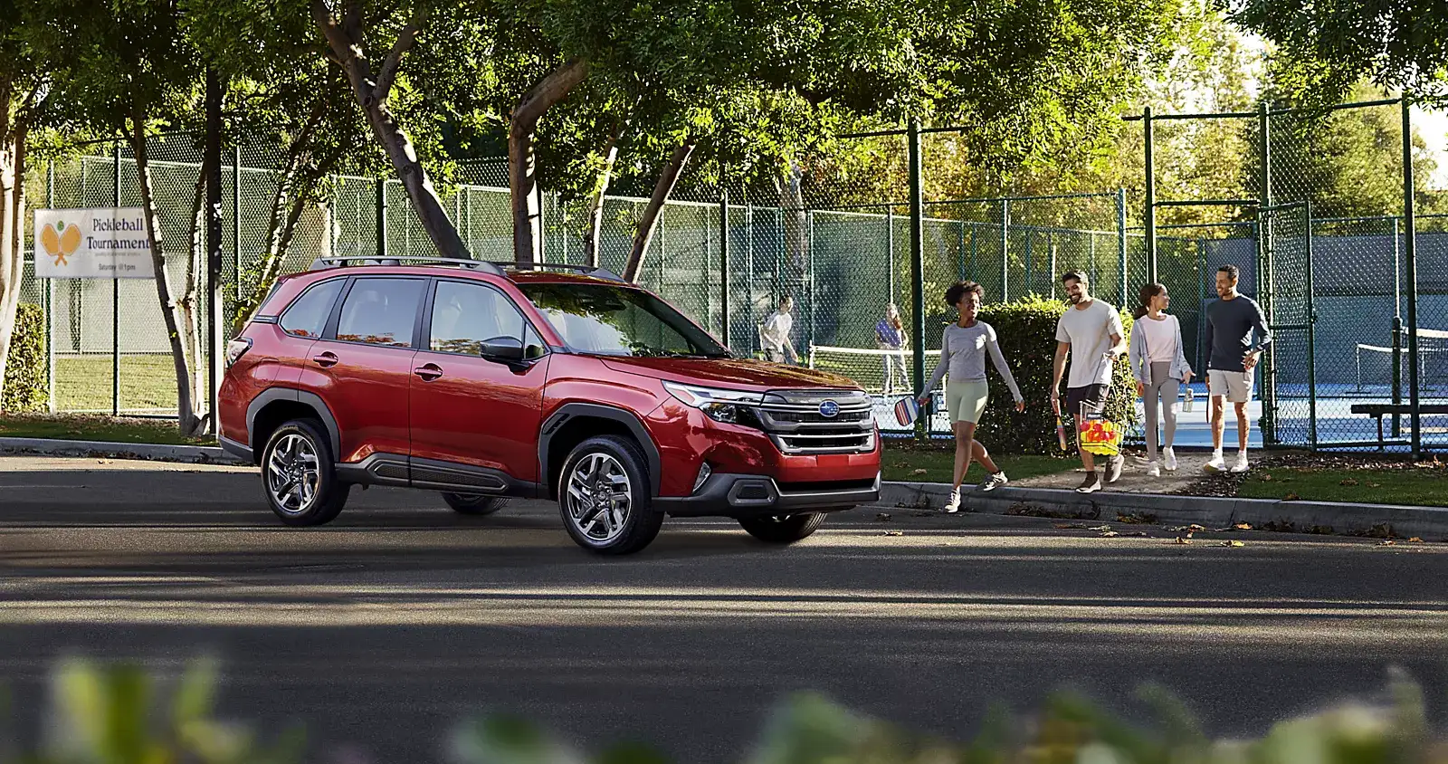Red Subaru Forester parked by a park with people walking