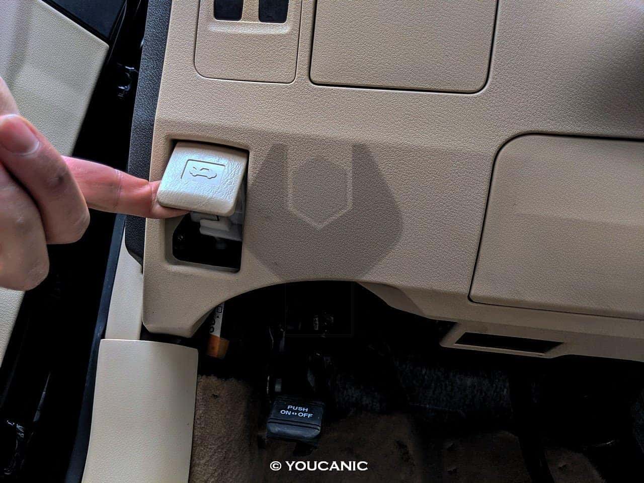 Hand pulling the hood release lever under a Subaru dashboard