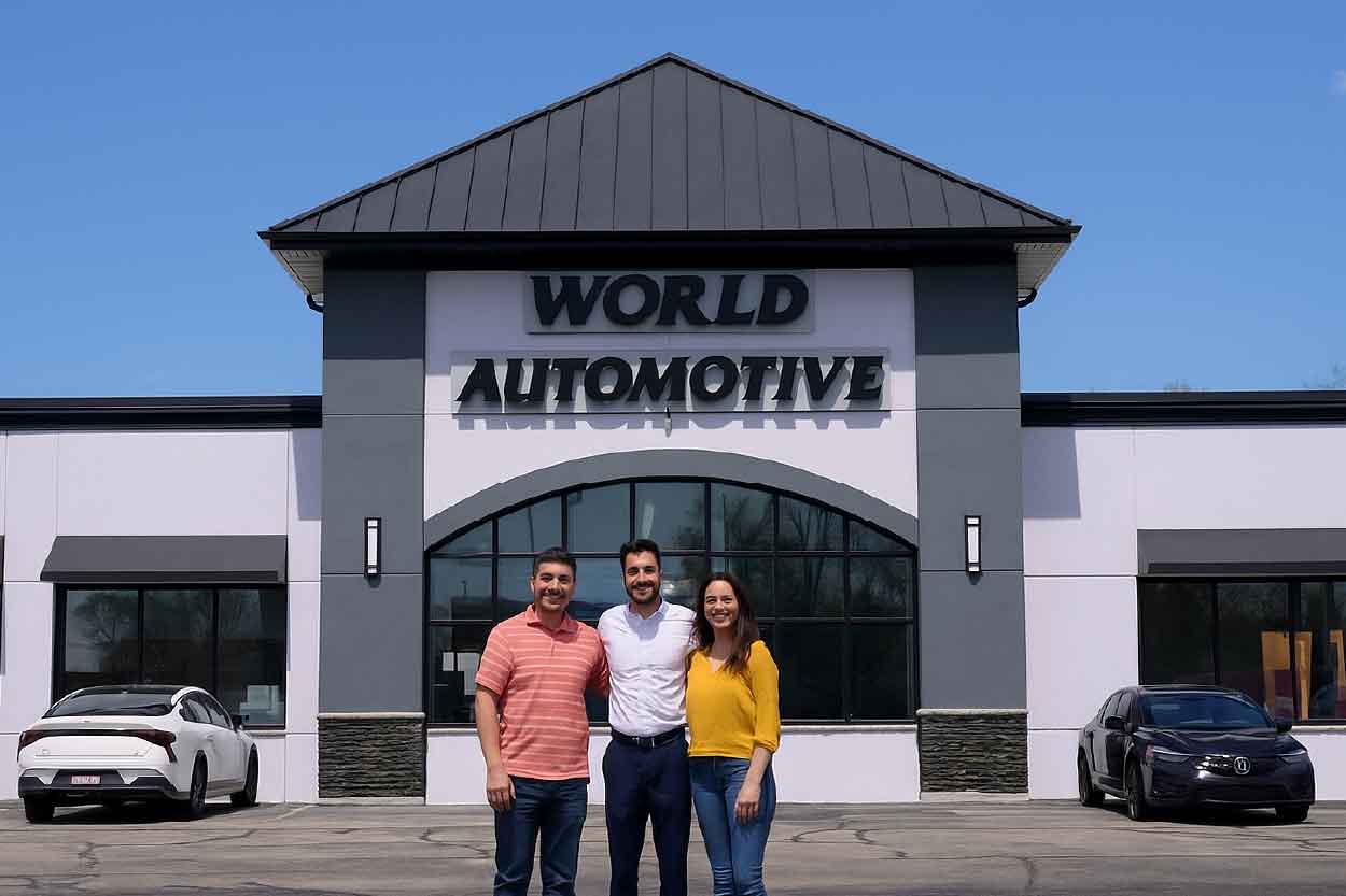 Image of a couple standing with a used car salesman standing outside the World Automotive Used Car Lot Front doors.