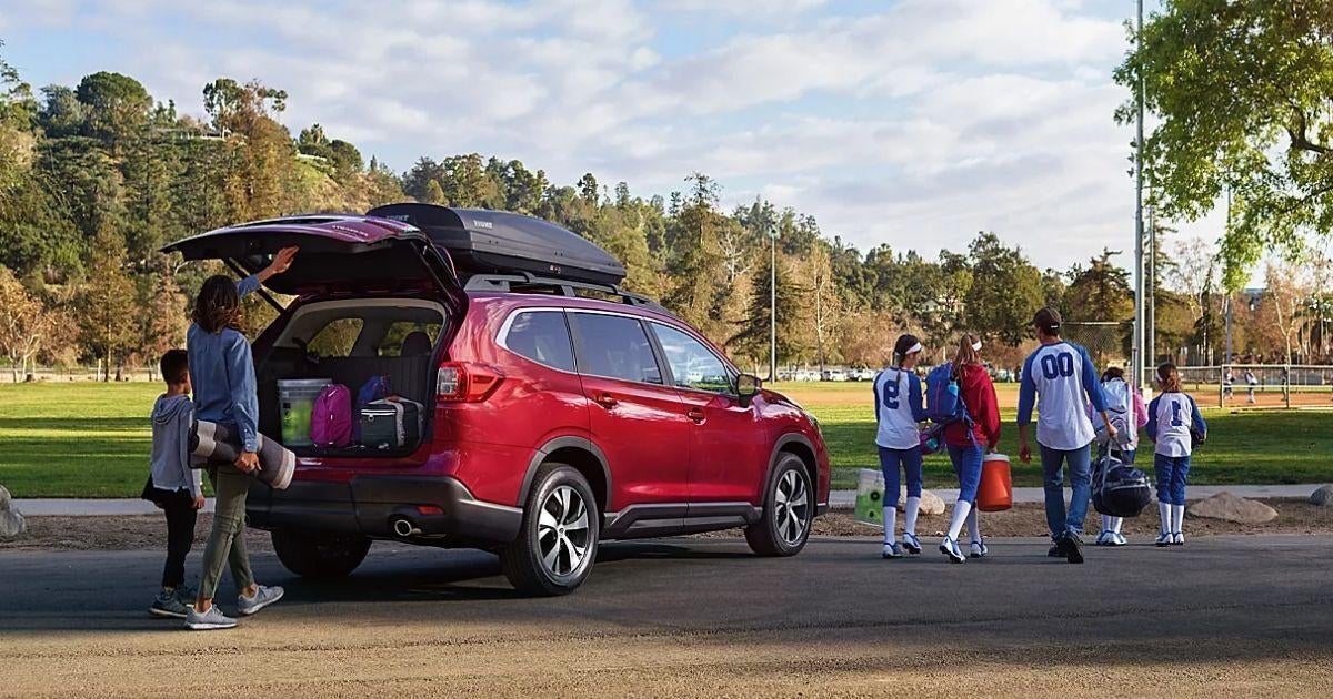 Family loading sports gear into the open rear cargo area of a red Subaru Ascent at a park