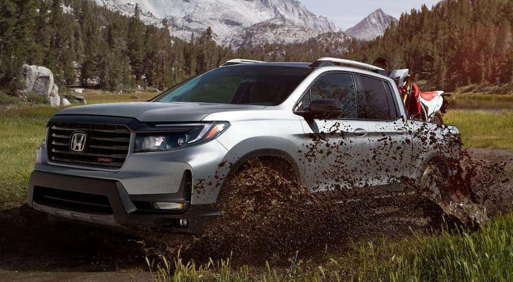 A silver 2025 Honda Ridgeline Sport angled right and driving through a mud puddle.