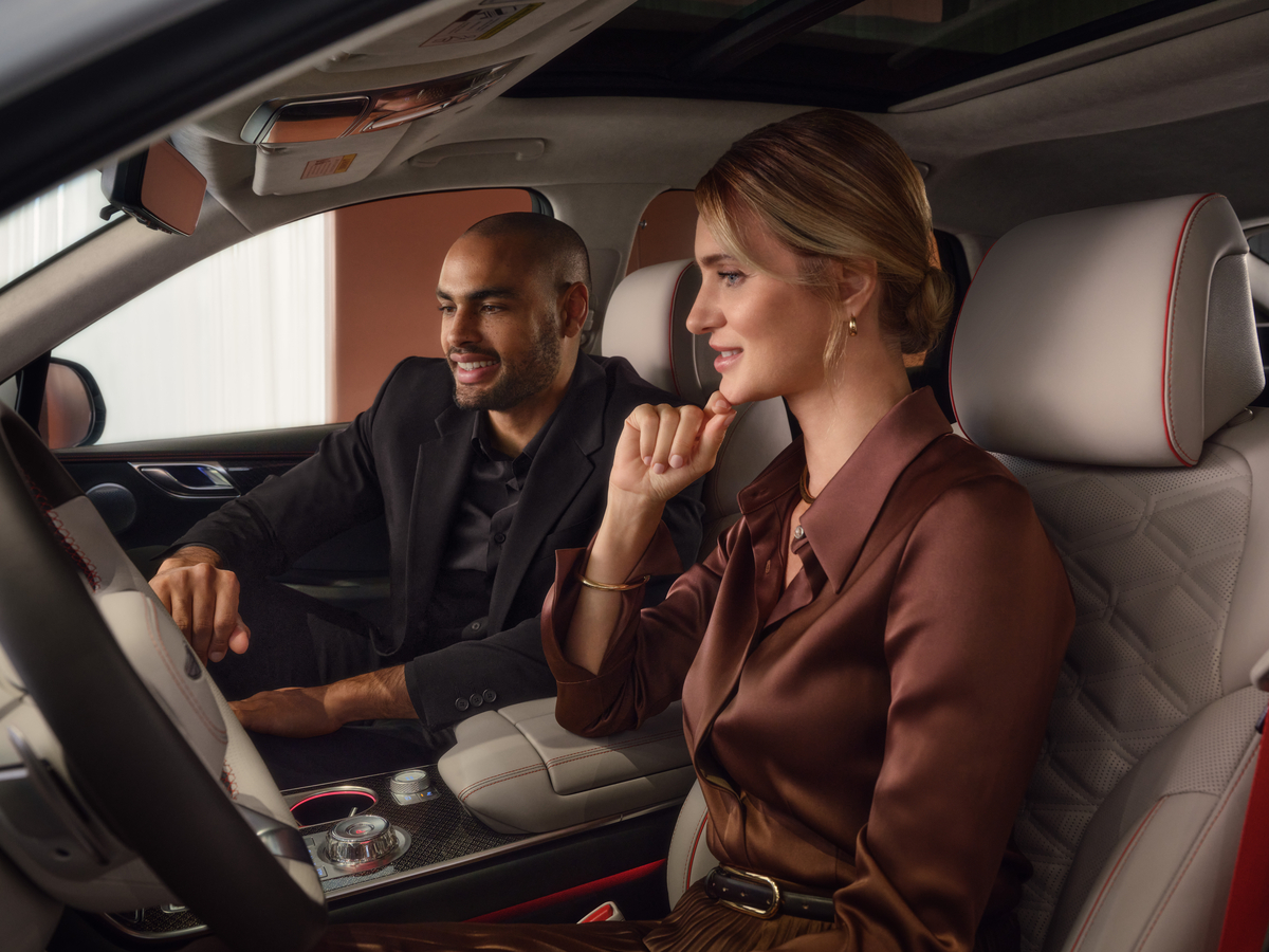 Interior view of a luxury genesis vehicle with two passengers exploring dashboard features