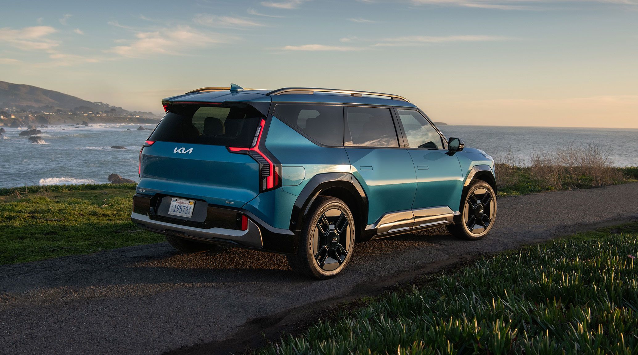 2026 Kia EV9 in blue, three-quarter back view, parked on a small road overlooking the ocean