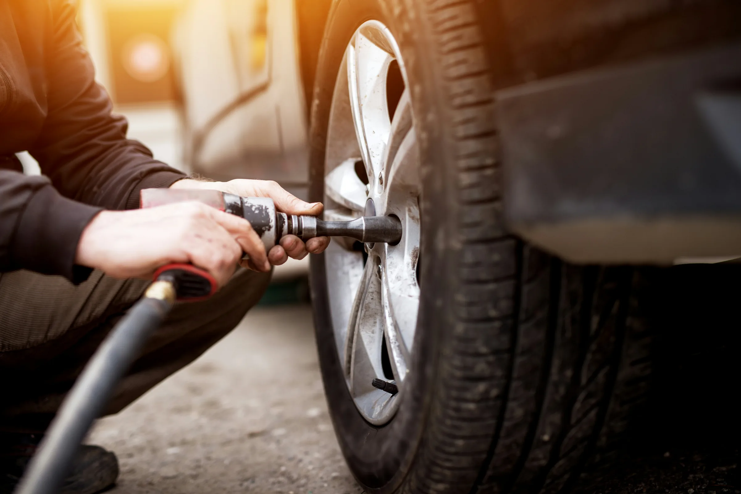 Technician using a pneumatic wrench to remove a wheel outdoors in sunlight. Tire Rotation Service Near Shawnee, KS